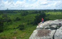 A woman sits on a rock overlooking a green landscape in Cameroon