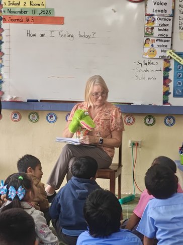 female teacher at the front of the class reading to a group of children who are sitting on the floor