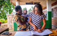 PCV Maya writes in log book with mother and baby looking on