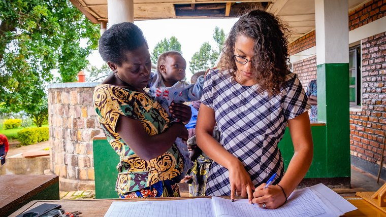 PCV Maya writes in log book with mother and baby looking on