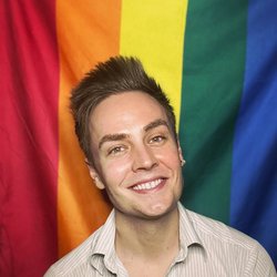 Returned Volunteer Chase sitting in front of the pride flag