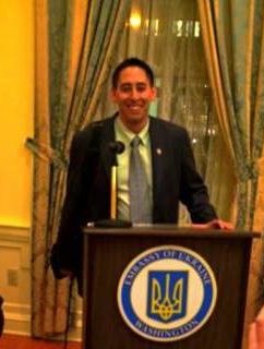 A white man stands at a podium, smiling.