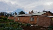 A rural Rwanda house in the foreground and a volcano in the background