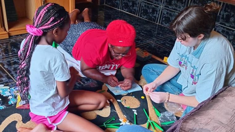 Chloe builds a Lego set with her host mom and sister while her host grandma watches TV.