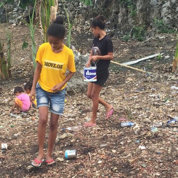 Two young women planting: one is looking for an open hole, the other covering up a hole with her foot.