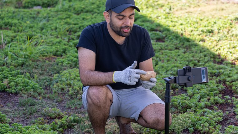 A young man points to a potato in front of his phone which is on a tripod