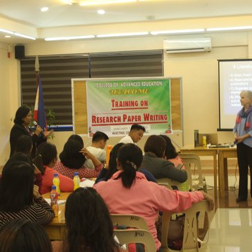 Group of people in a classroom with two people standing up and one with a microphone talking