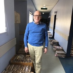 Man stands in a hallway besides stacks of paper files.
