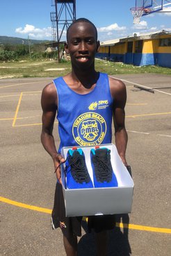 A Jamaican basketball player holds a box of shoes open on a basketball court.
