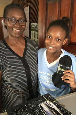 A Jamaican principal and her student holding up a pair of socks donated.