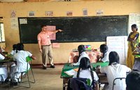Volunteer points to chalkboard in front of students