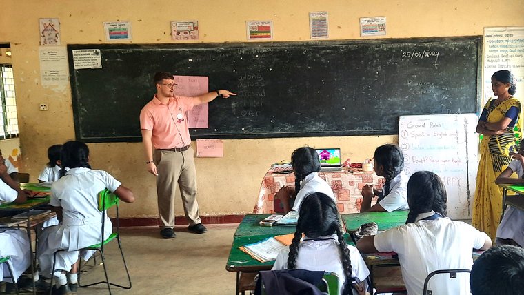 Volunteer points to chalkboard in front of students