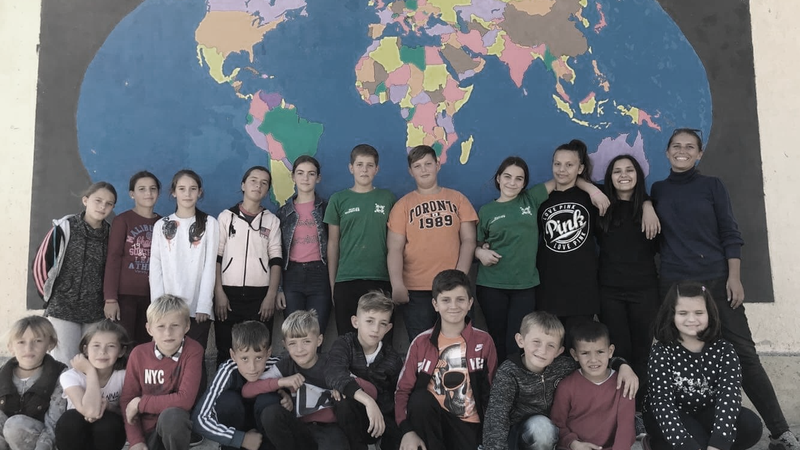 A group of students pose in front of world map mural they painted at their school.