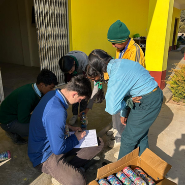 Students gather around Steven as he records the weight of their eco-bricks and enters it into the school wide competition.