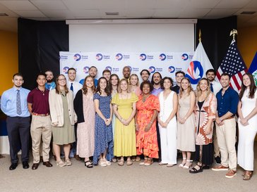 group of volunteers in front of a peace corps banner and flags