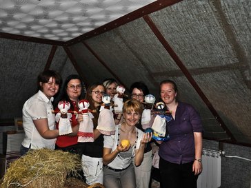 A group of women are in a room holding their straw dolls.