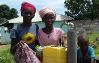 Two young girls stand in front of a newly installed water pump.