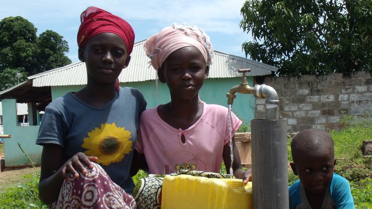 Two young girls stand in front of a newly installed water pump.
