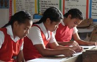 Three school girls in uniforms sit at their desks and read papers deep in concentration.