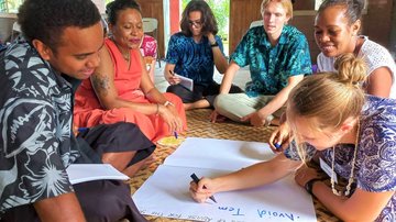 Group picture of volunteers and community members sitting together on the floor mat discussing a workshop topic