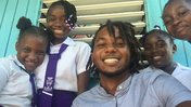 Male Trinidadian Teacher with dreads smiling beside Jamaican primary school students