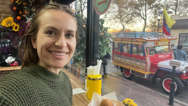 A young woman takes a selfie eating at window countertop.
