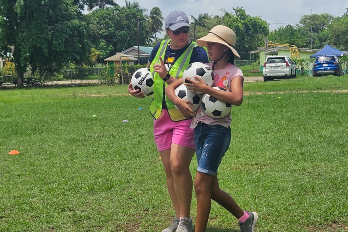 volunteer with girl and both carrying footballs to practice