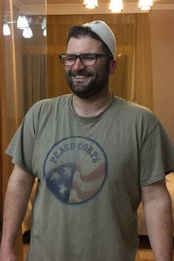 A man wearing a beige Peace Corps shirt smiles