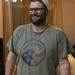 A man wearing a beige Peace Corps shirt smiles