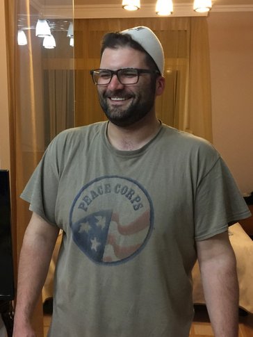 A man wearing a beige Peace Corps shirt smiles