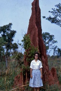A female stands beside a towering termite mound in Nigeria