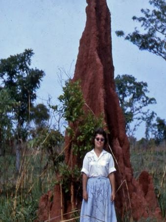A female stands beside a towering termite mound in Nigeria