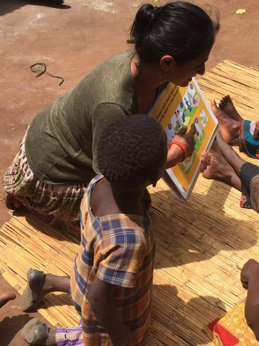 Woman kneeling on straw mat reading to children