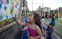 A young girl, hand covered in blue paint, adds her hand print to piece of paper with other colorful hand prints.