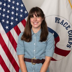 A woman in a light blue dress stands in front of the American flag