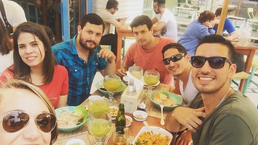 A group of friends take a selfie while sitting outside at a table, eating Peruvian food.