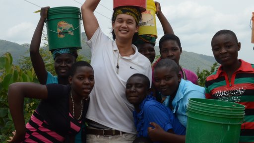 Education Volunteer Andrew carries water on his head with some students.