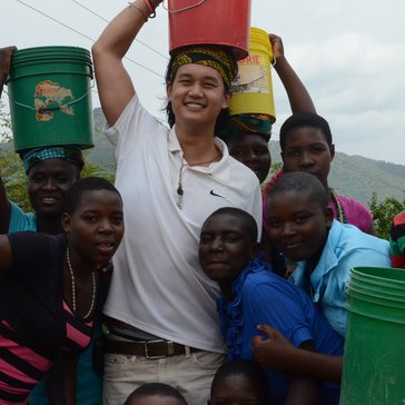 Education Volunteer Andrew carries water on his head with some students.