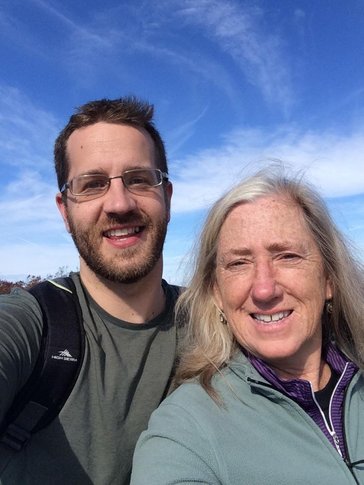 A young white male and his mother take a selfie outside.