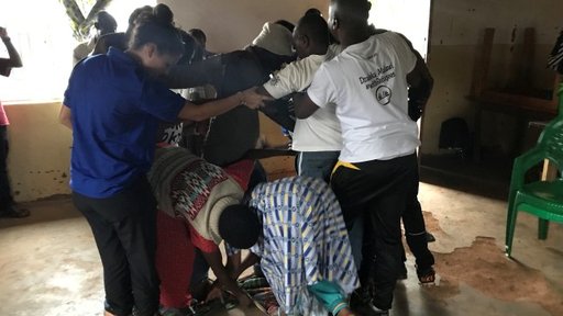 A group of Malawian teachers huddle together in a group inside of a classroom, preforming a teamwork activity