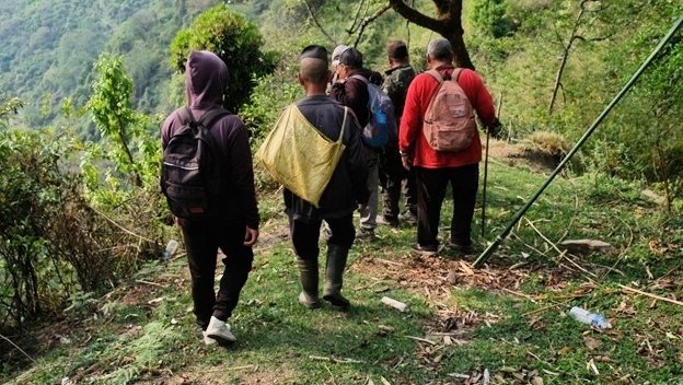 A small group walks along a narrow path to reach the point where a ladder is secured.