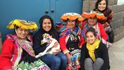 Fiorella sits with women in bright traditional Peruvian clothing with a small lamb on her lap