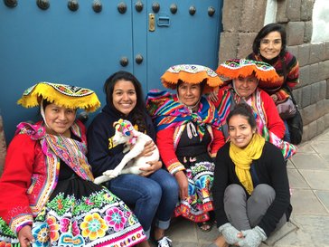 Fiorella sits with women in bright traditional Peruvian clothing with a small lamb on her lap