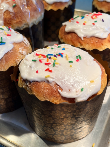 Baked bread in cupcake holders with white icing and rainbow sprinkles