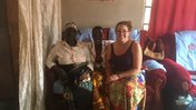 A white, female Volunteer sits smiling with two Malawian women on a sofa chair.