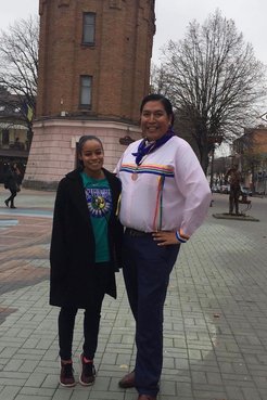 Two people of Indigenous heritage stand outside in their traditional clothing.