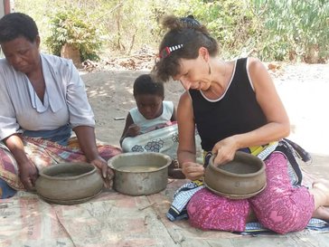 Birgit sits on a bamboo mat with a Malawian woman and a child as they hold and mold clay pots in their laps