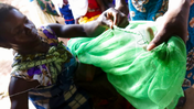 A Malawian woman sews up a hole in a green mosquito net.
