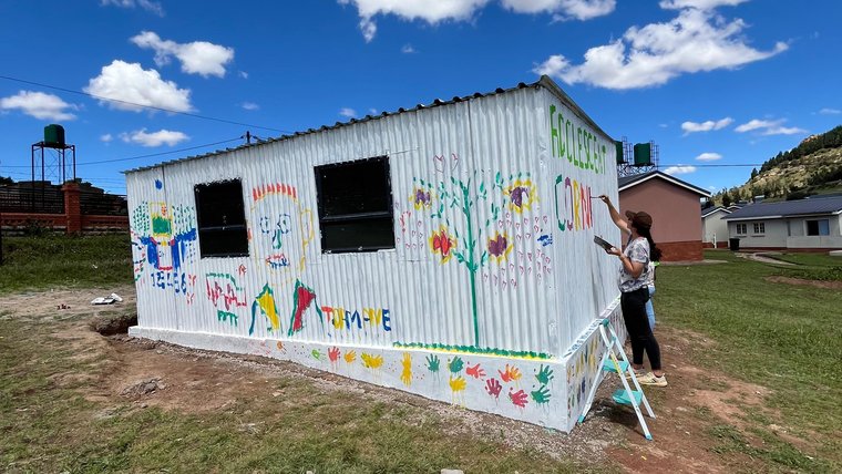 Volunteer Dylann paints sign for a newly established adolescent health space at a local health clinic in Lesotho.