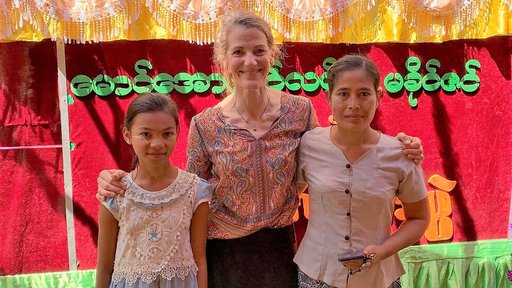 Two young women from Myanmar stand on either side of an older white woman, who is smiling.